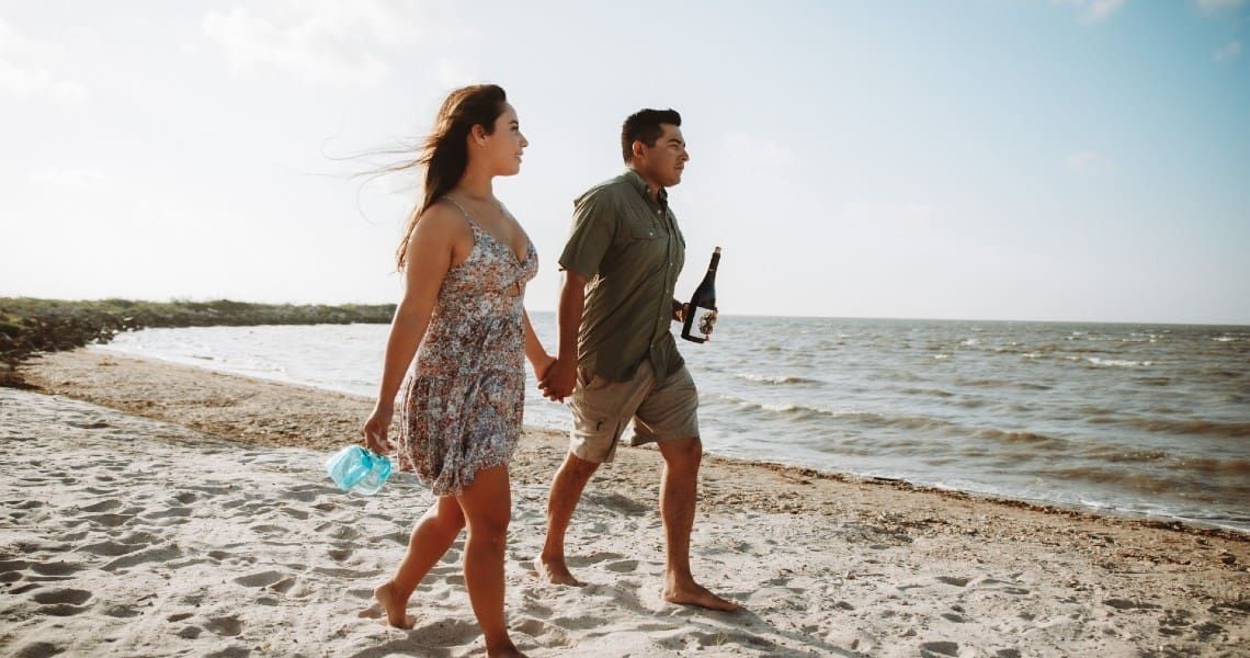 A couple is walking hand-in-hand along a sandy beach.