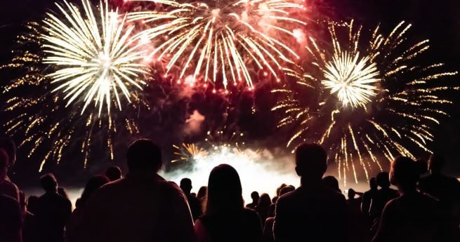 Silhouetted crowd watching a vibrant fireworks display against the night sky.