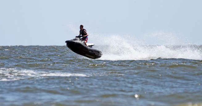 A person is riding a jet ski on the open water, captured in mid-air as they hit a wave.