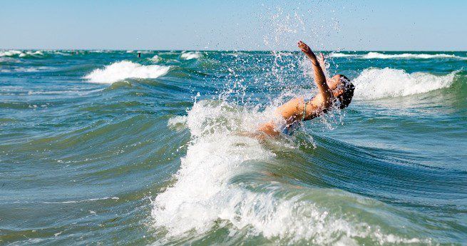 The image captures a person enjoying the ocean waves, with their body arched backward as they splash into the water.