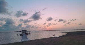 A serene sunset over a calm body of water, with a pier extending into the distance.