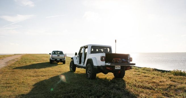 how to buy land in texas-vehicles on shore-2 (1) Two vehicles parked on a grassy shore near a body of water under a bright sun.