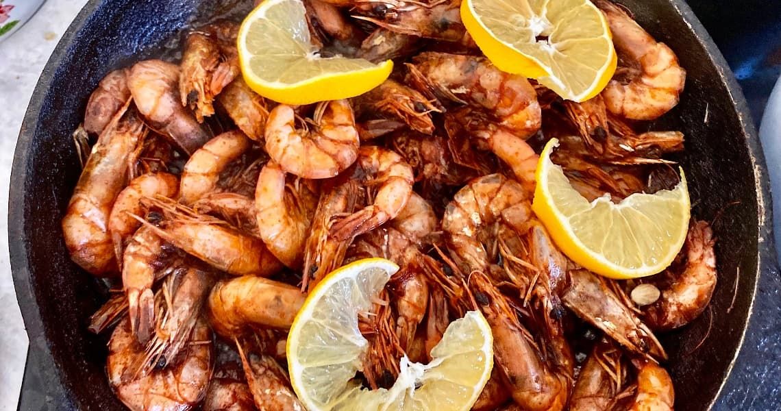 A skillet filled with seasoned, cooked shrimp garnished with fresh lemon wedges.